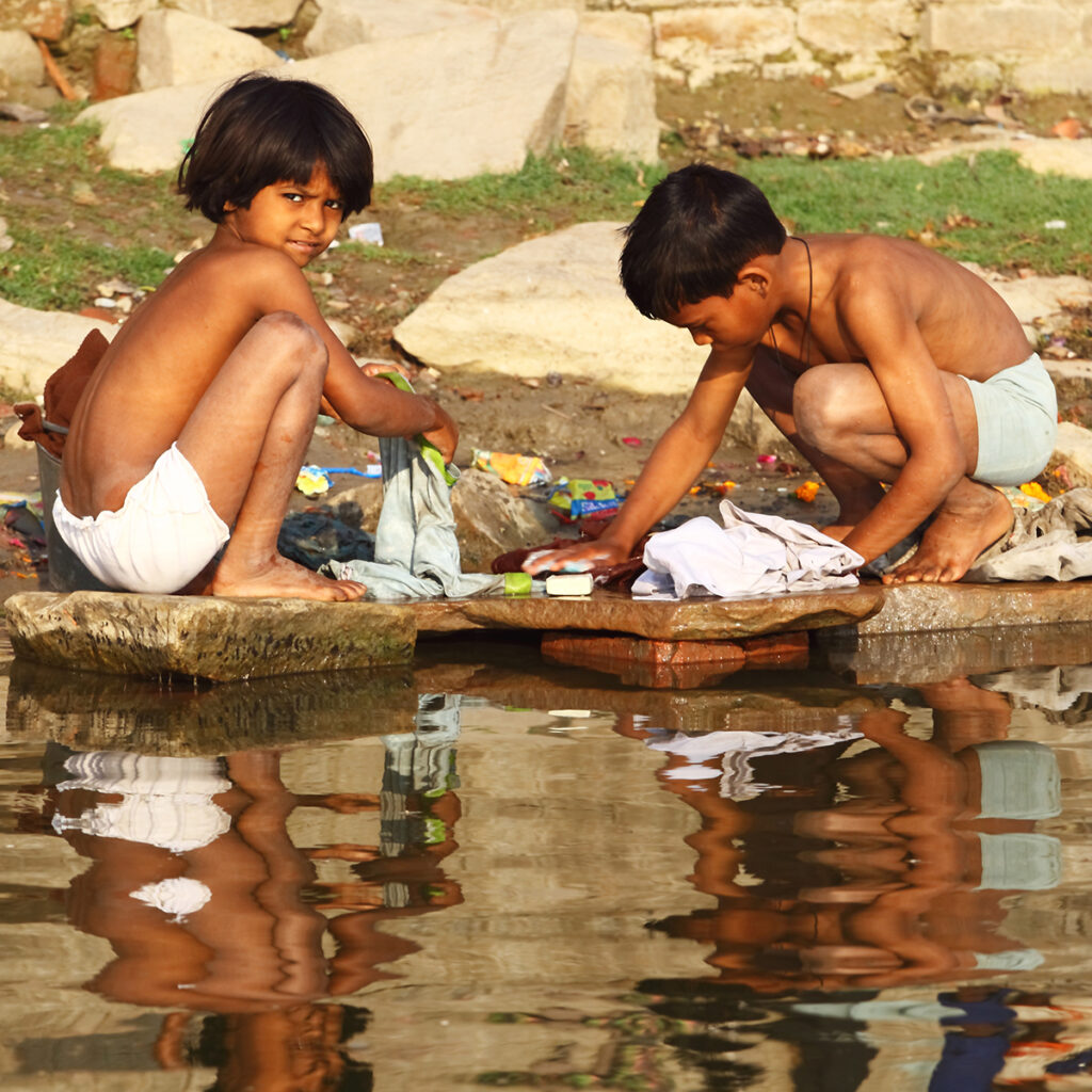 Two young kids do the family washing on the bank of the Ganges River.